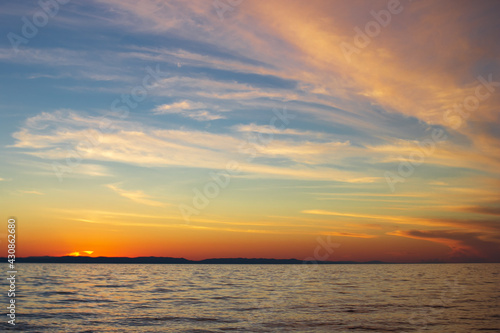 Light clouds on blue sky in yellow pink tones, sunset on lake, beautiful scenic seascape of calm sea in sundown dusk © Clara_Sh.