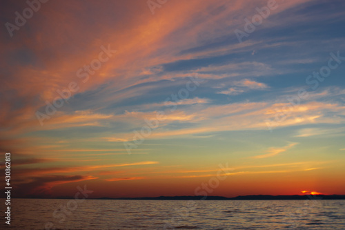 Long dramatic majestic clouds on blue sky with yellow pink tones in sunset blazing  scenic seascape of calm sea in dusk