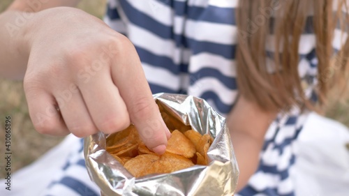 The girl eats chips in the city park in the summer. The girl eats chips in the city park in the summer. Package with chips close-up.