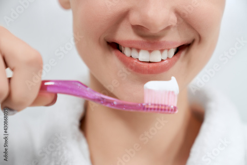 Close up young beautiful woman cleaning teeth with pink toothbrush in bathroom. Concept of care for health at home with special toothpaste at home. 
