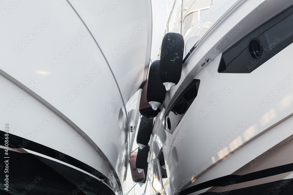 Two white luxury yachts stand side by side in dry dock with fenders on the sides. Two white luxury yachts stand side by side in dry dock with fenders on the sides.