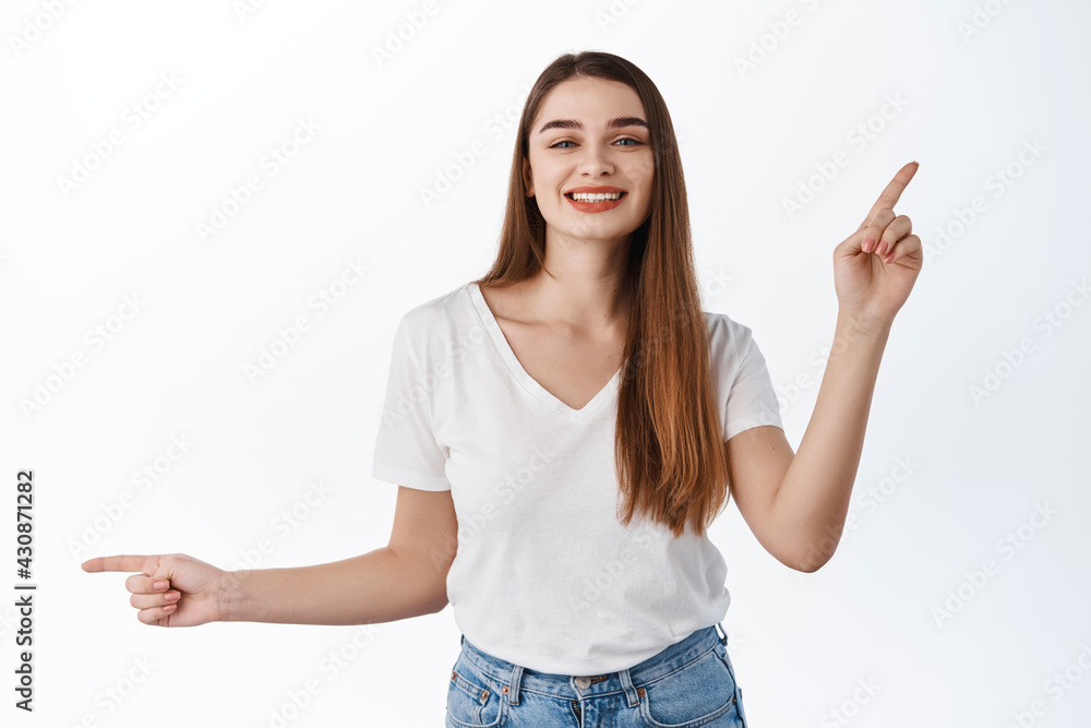 Beautiful cheerful girl, smiling and dancing, pointing fingers sideways at two promo deals, showing banners choices, best promo offers, standing over white background Beautiful cheerful girl, smiling and dancing, pointing fingers sideways at two promo deals, showing banners choices, best promo offers, standing over white background