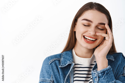 Beauty. Happy young millennial girl holding hand on face, laughing and smiling carefree, enjoying natural clean and fresh skin feeling after skincare product cosmetic, standing over white background