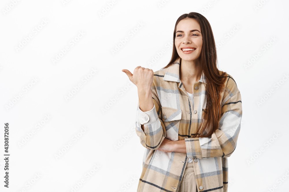 Beautiful smiling woman pointing and looking aside, showing logo, stare pleased at copy space with product promo offer, standing against white background Beautiful smiling woman pointing and looking aside, showing logo, stare pleased at copy space with product promo offer, standing against white background