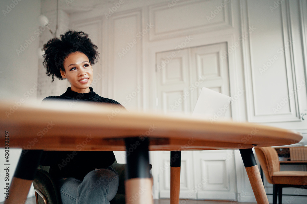 Typing a message to friends sitting in a chair. Portrait of a woman of Afro appearance using a laptop in her hands. Writes a message to friends sitting on the couch. Stylish interior in the apartment. Typing a message to friends sitting in a chair. Portrait of a woman of Afro appearance using a laptop in her hands. Writes a message to friends sitting on the couch. Stylish interior in the apartment.