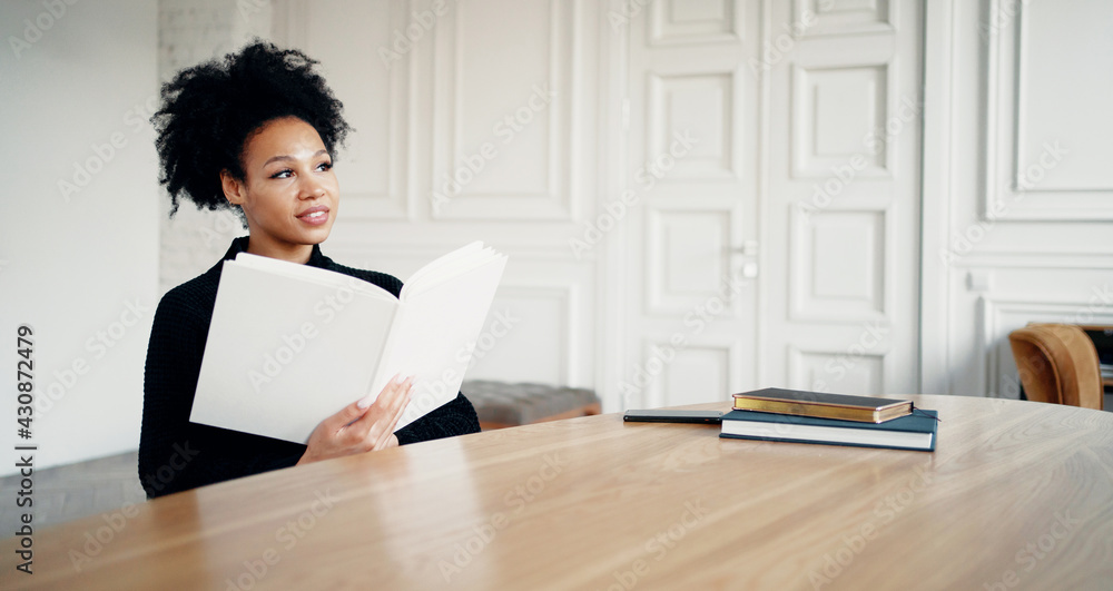 In the college library. The student is a smart African American looking woman.Reading holding a book textbook white cover blank. In the college library. The student is a smart African American looking woman.Reading holding a book textbook white cover blank.