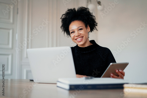 Employee smiles works via the Internet from the office in a coworking space. The manager prints the text on the computer laptop. In his hands, he holds a tablet with statistics about the new project.