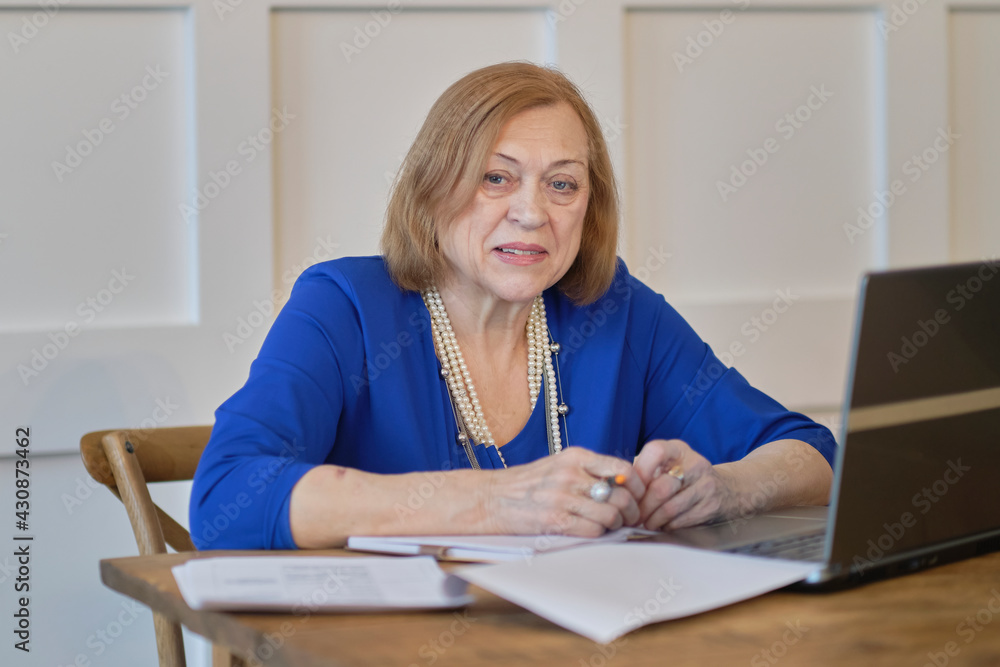 Pensioner using laptop for internet banking Mature lady sitting at work typing a notebook computer in an home office. Mature woman working with documents at table in home Pensioner using laptop for internet banking Mature lady sitting at work typing a notebook computer in an home office. Mature woman working with documents at table in home