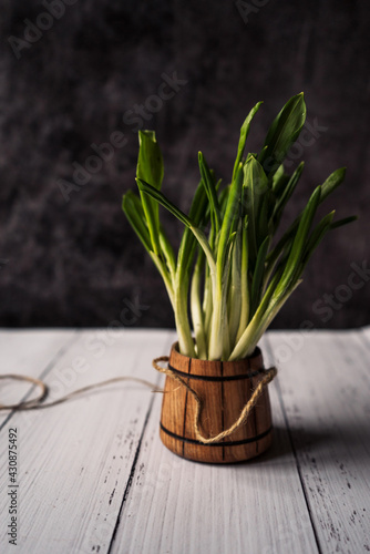 a bunch of fresh eco-friendly and healthy greens in a wooden glass on a white wooden background. Place for text 1