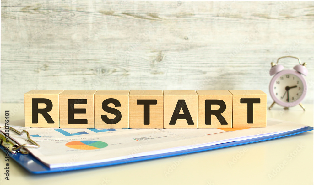 Wooden cubes lie on a folder with financial charts on a gray background. The cubes make up the word RESTART. Wooden cubes lie on a folder with financial charts on a gray background. The cubes make up the word RESTART.