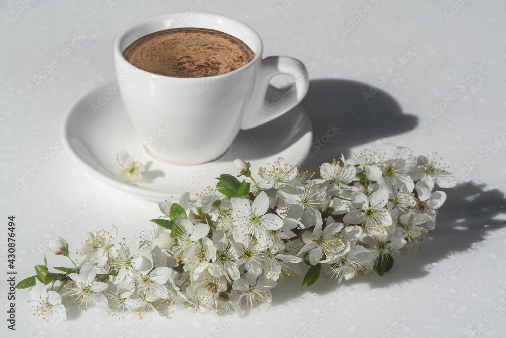 Cup of coffee and branch of blossoming cherry with white flowers in natural morning sunlight. Spring concept. Minimal style.