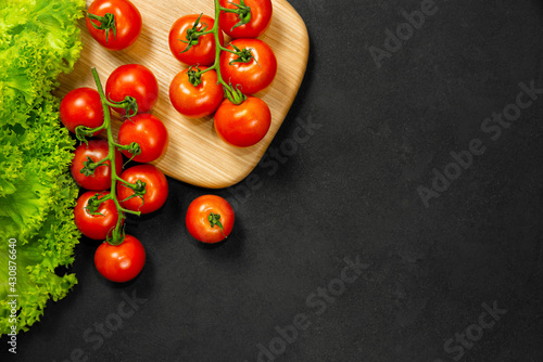 Fresh lettuce and cherry tomatoes on a wooden board on a dark background.