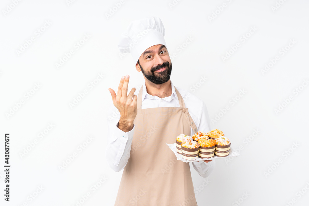 Young man holding muffin cake over isolated white background inviting to come with hand. Happy that you came