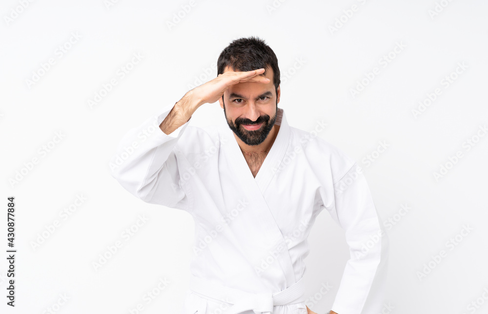 Young man doing karate over isolated white background looking far away with hand to look something Young man doing karate over isolated white background looking far away with hand to look something