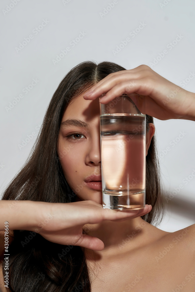 Young asian girl hiding face behind glass with water - obrazy, fototapety, plakaty 