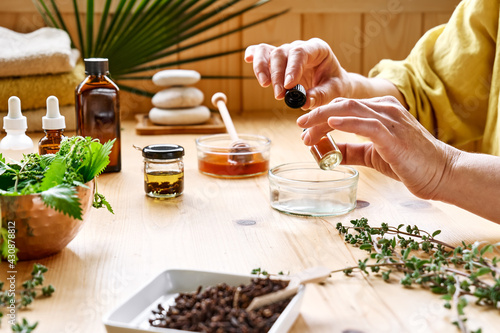 Woman prepares aromatherapy session at the table with essential oil diffuser medical herbs, different types of oils and essences. Aromatherapy and alternative medicine concept. Natural remedies. photo