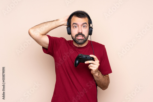 Man playing with a video game controller over isolated wall frustrated and takes hands on head