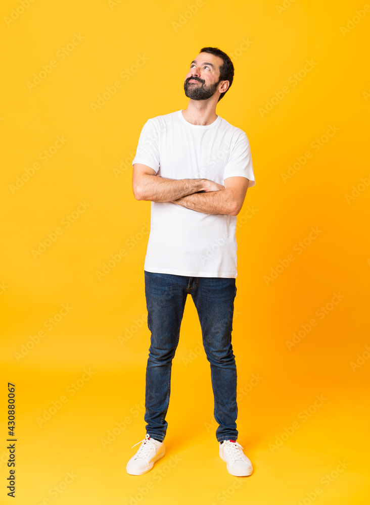 Full-length shot of man with beard over isolated yellow background looking up while smiling Full-length shot of man with beard over isolated yellow background looking up while smiling