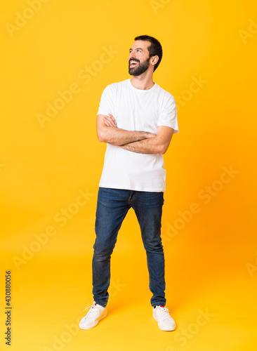Photos Full-length shot of man with beard over isolated yellow background happy and smi