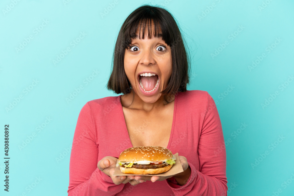 Young brunette woman holding a burger over isolated background Young brunette woman holding a burger over isolated background