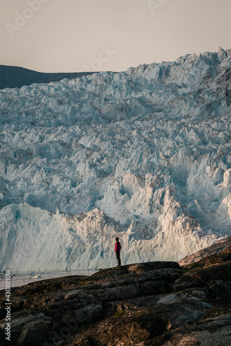 Unidentified People sitting standing in front of huge glacier wall of ice. Eqip Sermia Glacier Eqi glacier in Greenland called the calving glacier during midnight sun. Hikers during travel and