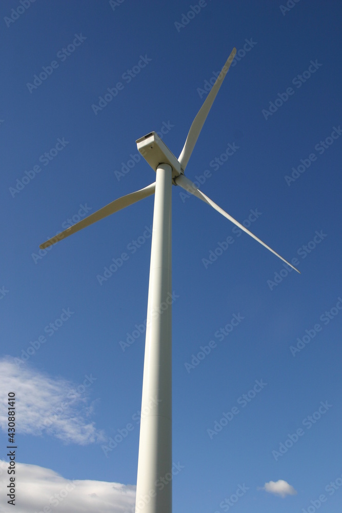 A Wind Turbine Creating Electricity from Wind Power using Induction with a Blue Sky in the Background A Wind Turbine Creating Electricity from Wind Power using Induction with a Blue Sky in the Background