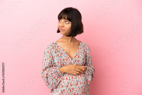 Young pregnant woman over isolated pink background making doubts gesture looking side