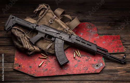 A classic Soviet military rifle AK in a modern body kit. The carbine and cartridges to it are on near the military backpack and the target for shooting. Weapons on a wooden table. photo