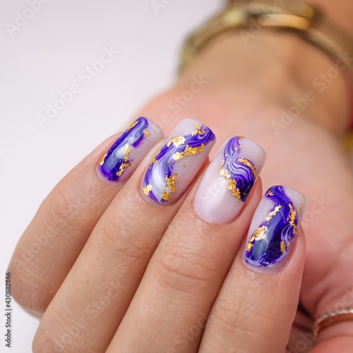 A well-groomed female hand on a white background, a manicure with a blue and light gel polish with the addition of gold.