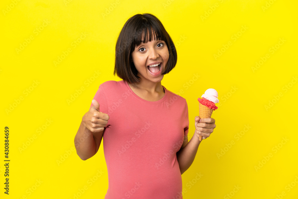 Pregnant woman holding a cornet ice cream isolated on yellow background with thumbs up because something good has happened Pregnant woman holding a cornet ice cream isolated on yellow background with thumbs up because something good has happened