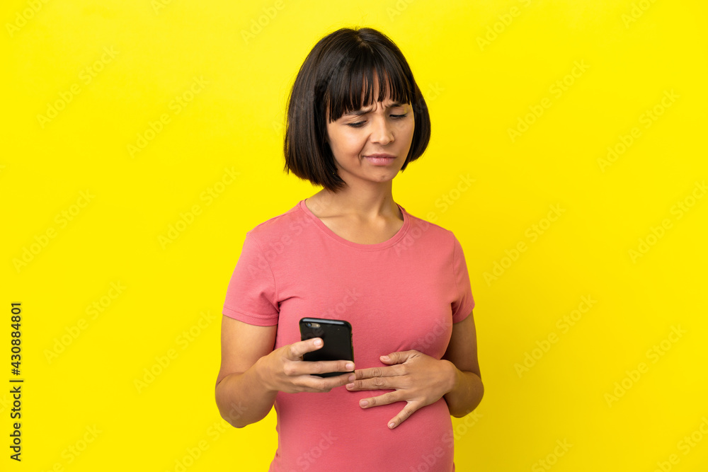 Young mixed race pregnant woman isolated on yellow background using mobile phone Young mixed race pregnant woman isolated on yellow background using mobile phone