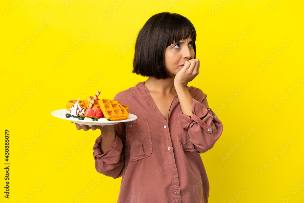 Pregnant woman holding waffles isolated on yellow background having doubts Pregnant woman holding waffles isolated on yellow background having doubts