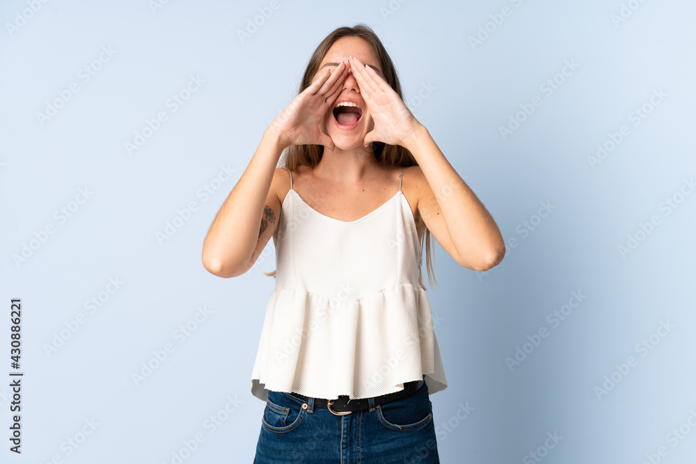 Young Lithuanian woman isolated on blue background shouting and announcing something Young Lithuanian woman isolated on blue background shouting and announcing something