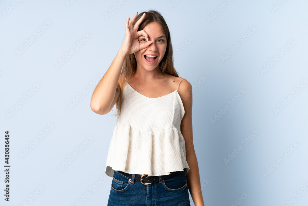 Young Lithuanian woman isolated on blue background showing ok sign with fingers Young Lithuanian woman isolated on blue background showing ok sign with fingers