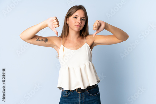 Young Lithuanian woman isolated on blue background showing thumb down with two hands © luismolinero