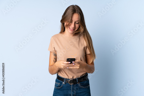 Young Lithuanian woman isolated on blue background sending a message with the mobile