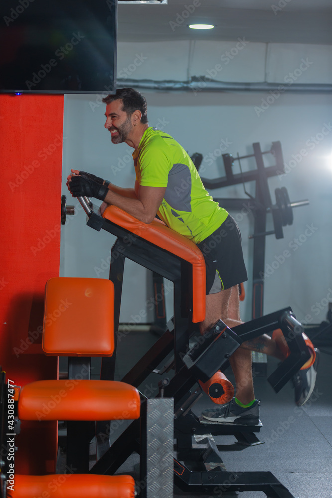 Side view of a middle-aged man with a yellow fluorescent shirt exercising on the machine for legs. Side view of a middle-aged man with a yellow fluorescent shirt exercising on the machine for legs.