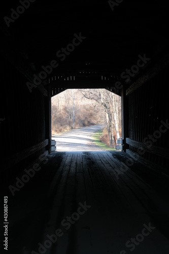 Covered bridge dirt road with trees and grass edge.