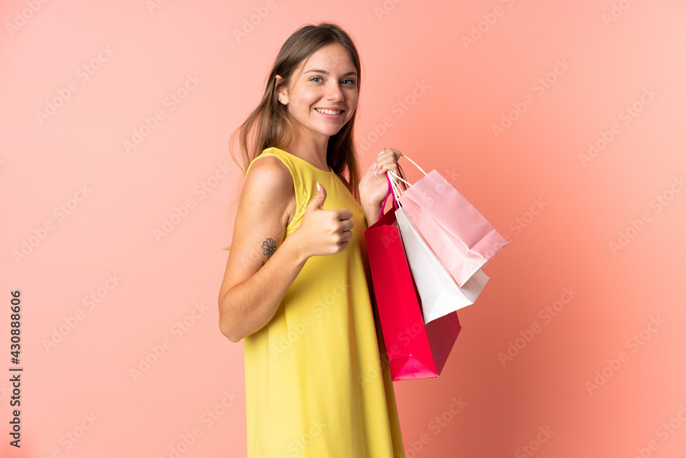 Young Lithuanian woman isolated on pink background holding shopping bags and with thumb up