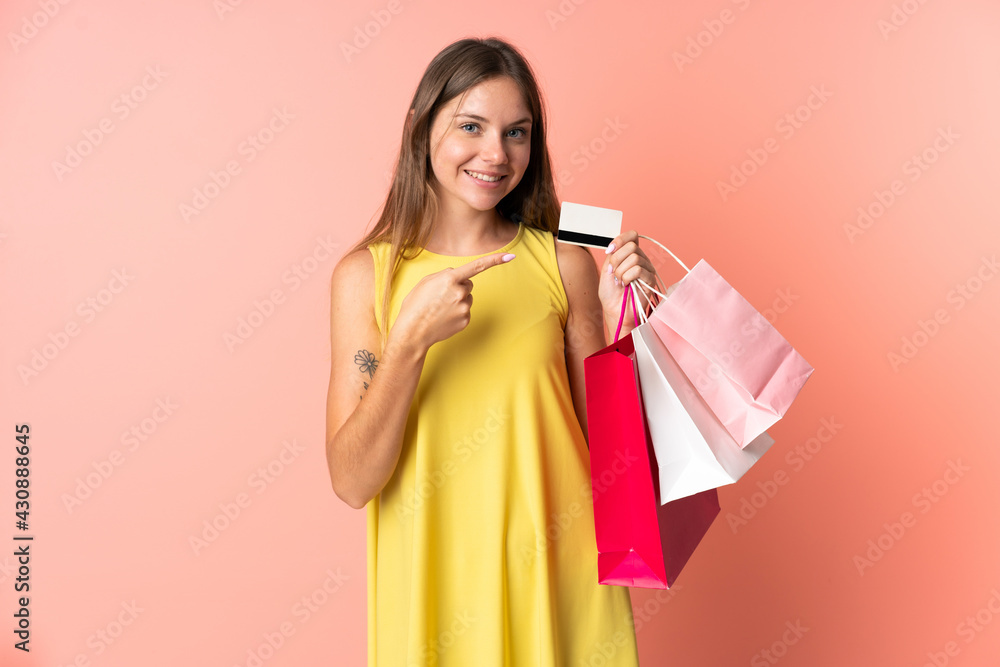Young Lithuanian woman isolated on pink background holding shopping bags and a credit card Young Lithuanian woman isolated on pink background holding shopping bags and a credit card