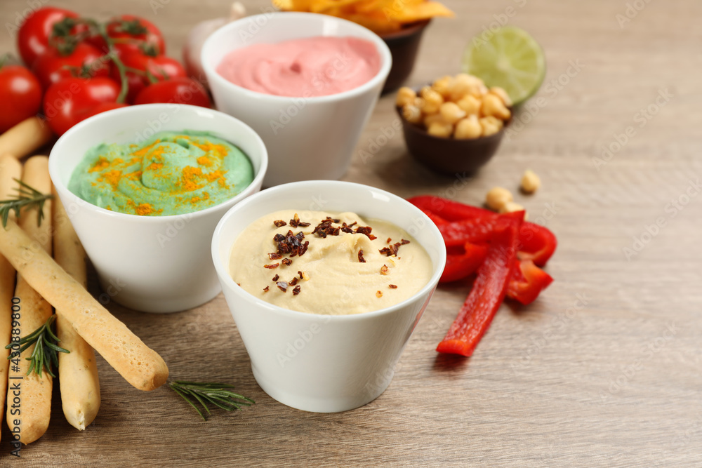 Different kinds of tasty hummus served with bread sticks on wooden table Different kinds of tasty hummus served with bread sticks on wooden table