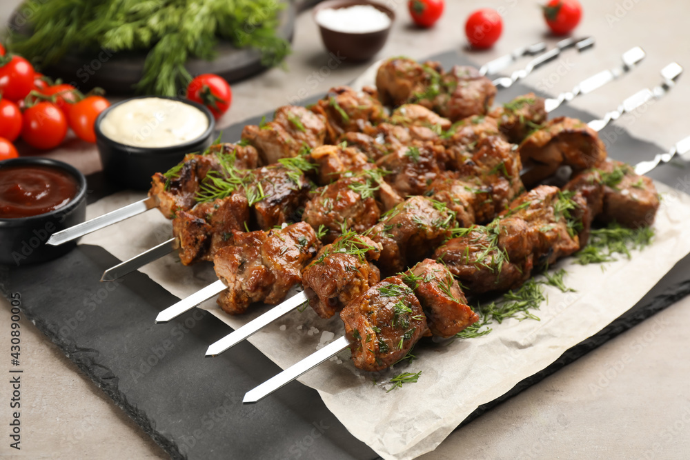Metal skewers with delicious meat served on light grey table