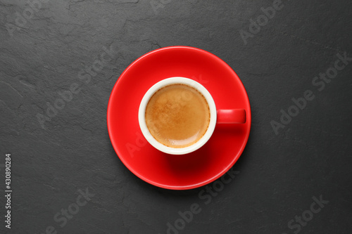 Aromatic coffee in red cup on black background, top view