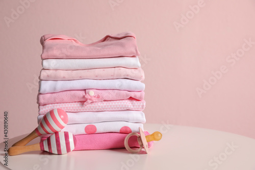 Stack of clean girl's clothes, pacifier and rattles on table. Space for text