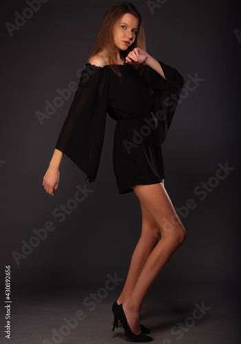 Full-length fashion portrait on a dark background of a beautiful female model wearing a little black dress