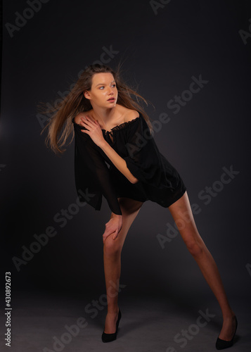 Full-length picture of an attractive sexy young female model posing isolated on a dark background with black dress