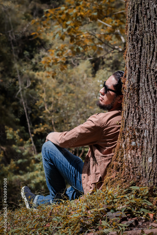 Hombre joven reposando sobre árbol en medio del bosque