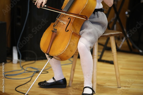 A little girl plays the cello with a bow.An old wooden musical instrument between the legs of a sitting child in white tights.Close-up image