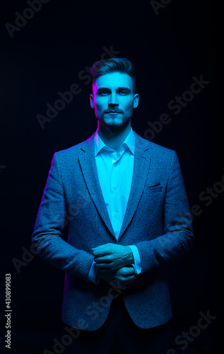 Young handsome model posing in a studio in a trendy neon light. Fashionable man in a stylish suit. Vibrant color. Bright colorful light effects. Disco style. Overlay. Gel filter. Supersaturated
