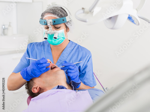 adult dentist checking teeth of patient male sitting in medical center